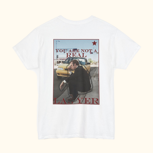White t-shirt with graphic design of a man sitting on a street and text 'YOU ARE NOT A REAL LAWYER' on a white background.